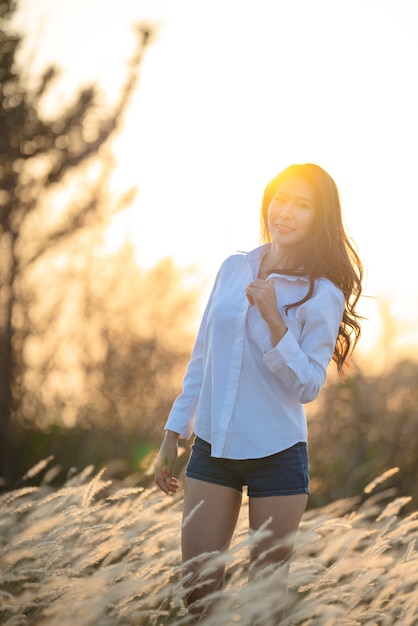 Jeune femme heureuse en jolie robe d'été debout dans le champ dans la lumière du coucher du soleil