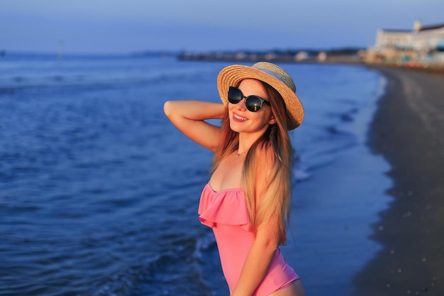 Jeune femme heureuse en maillot de bain rose et lunettes de soleil et canotier S