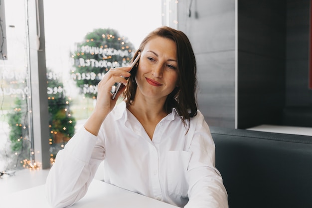 Jeune femme heureuse parlant sur un téléphone portable dans un café, une dame avec un beau sourire parlant sur un téléphone portable alors qu'elle était assise dans un café pendant le déjeuner