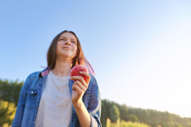 Jeune femme heureuse avec pomme rouge, fille mordant une pomme, fond de paysage naturel coucher de soleil, nourriture naturelle saine