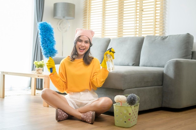 Jeune femme heureuse portant des gants jaunes et tenant un panier de produits de nettoyage dans le salon