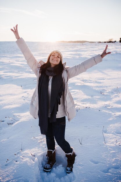 Photo jeune femme heureuse en randonnée dans la montagne enneigée portant un manteau moderne au coucher du soleil saison d'hiver nature