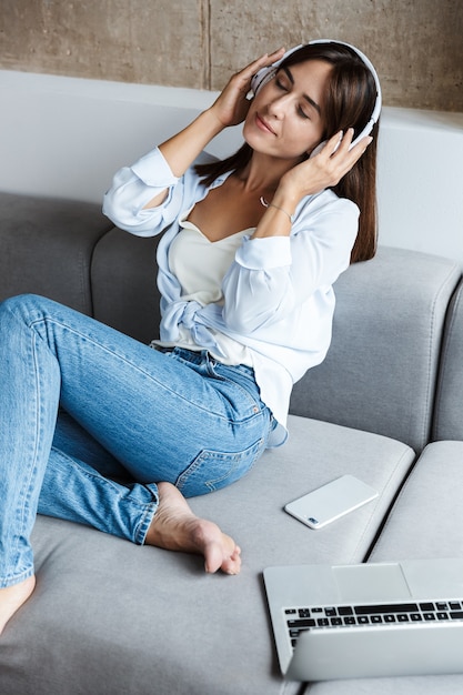 jeune femme heureuse et relaxante à l'intérieur à la maison s'asseoir sur un canapé dans le salon en écoutant de la musique avec des écouteurs.