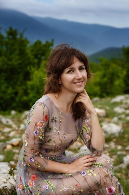 Jeune femme heureuse en robe longue à flanc de montagne Fille sur la nature sur fond de ciel bleu Photo de mode