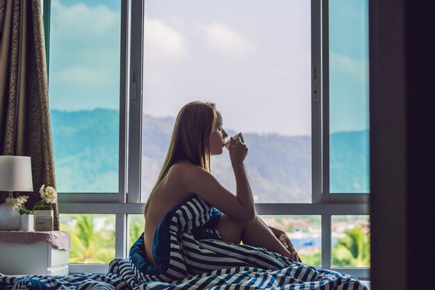 Jeune femme heureuse s'est réveillée le matin dans la chambre près de la fenêtre avec de belles vues sur la montagne