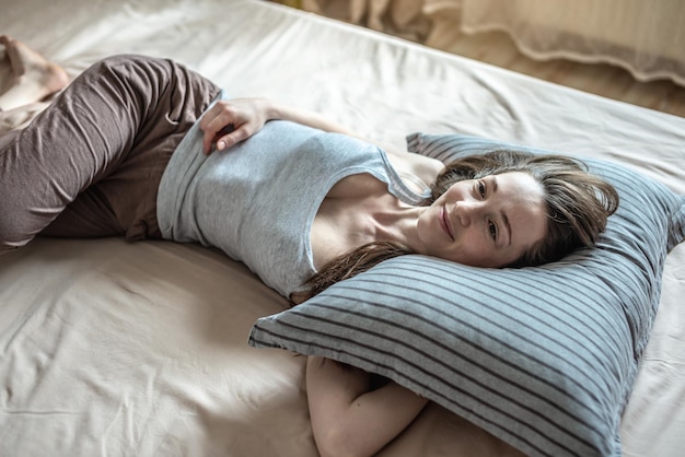 Jeune femme heureuse s'est réveillée le matin et est allongée dans son lit avec plaisir Concept de confort de sommeil sain et d'un début agréable pour une nouvelle journée