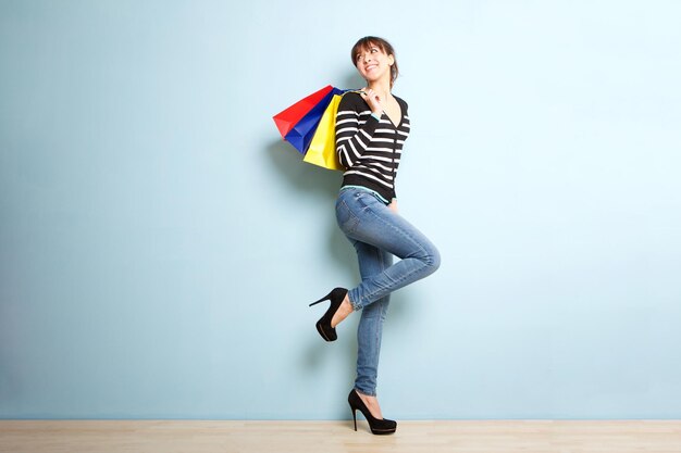 Une jeune femme heureuse avec des sacs d'achat sur un fond bleu.