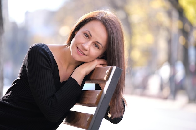 Jeune femme heureuse se reposant sur un banc de rue de la ville par une chaude journée d'automne. Bien-être et repos du concept de précipitation quotidienne.