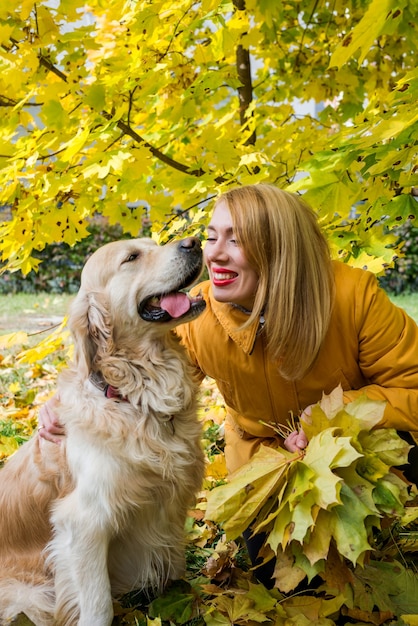 Jeune femme heureuse avec son retriever parmi les feuilles d'automne jaunes.