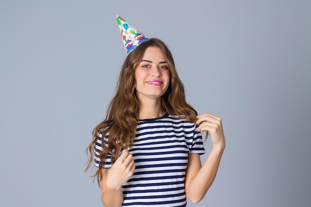 Jeune femme heureuse en T-shirt dépouillé et casquette de célébration faisant la moustache de ses longs cheveux