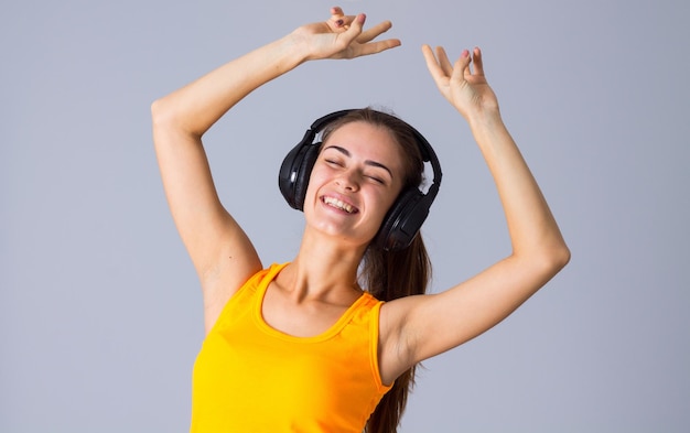 Jeune femme heureuse en T-shirt jaune écoutant de la musique dans des écouteurs noirs en studio