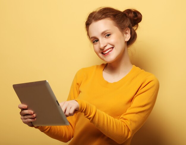 Jeune femme heureuse avec tablet pc sur fond jaune