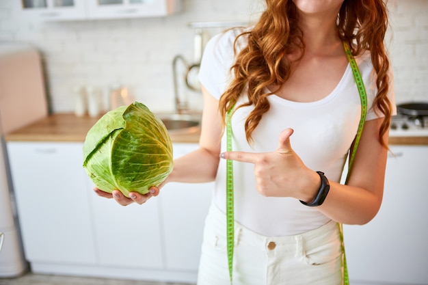 Jeune femme heureuse tenant le chou dans la belle cuisine avec des ingrédients frais verts à l'intérieur. Alimentation saine et concept de régime. Perdre du poids