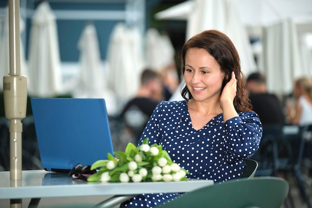 Jeune femme heureuse travaillant à distance sur un ordinateur portable assis à une table de restaurant en plein air Faire des affaires en ligne concept