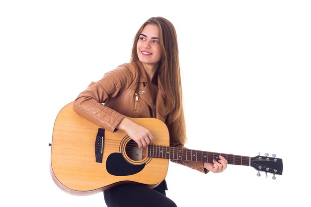 Jeune femme heureuse en veste marron et pantalon noir tenant une guitare sur fond blanc en studio