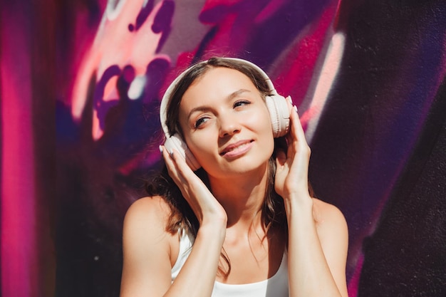 Une jeune femme heureuse vêtue d'un haut blanc et d'un casque jupe violette écoutant de la musique dansant sur