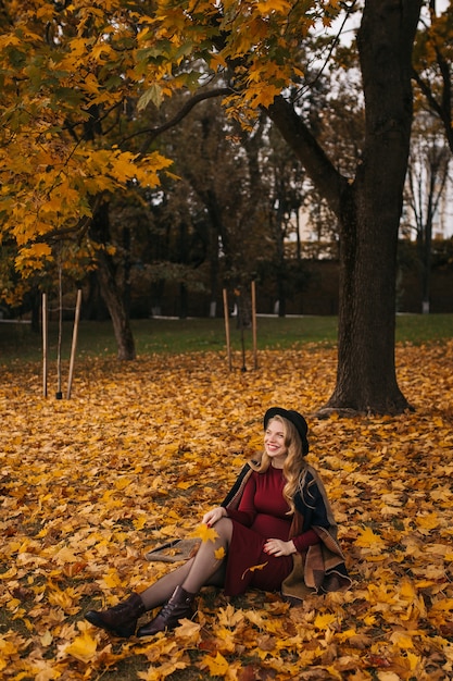 Une jeune femme heureuse vêtue d'une robe rouge et d'un chapeau noir posant dans le parc de la ville en mode jour d'automne...