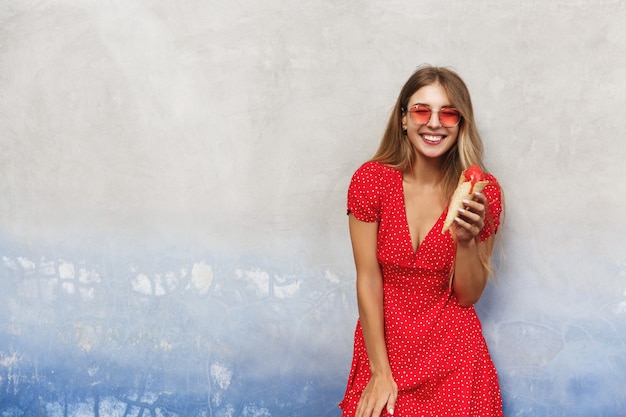 Jeune femme heureuse voyageant, manger de la crème glacée sucrée en vacances d'été, s'appuyer sur le mur