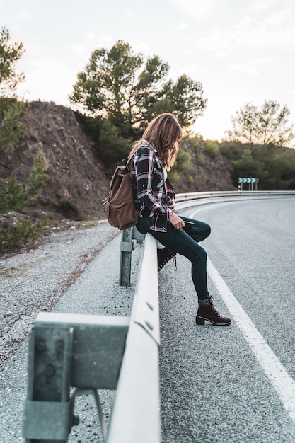 Jeune femme hip avec son sac à dos faisant de l'auto-stop sur la route en attendant une voiture. Concept d'exploration et d'aventures.