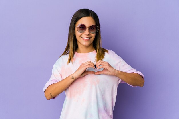 Jeune femme hippie isolée sur mur violet souriant et montrant une forme de coeur avec les mains.