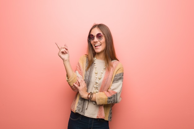 Jeune femme hippie sur mur rose pointant vers le côté avec le doigt