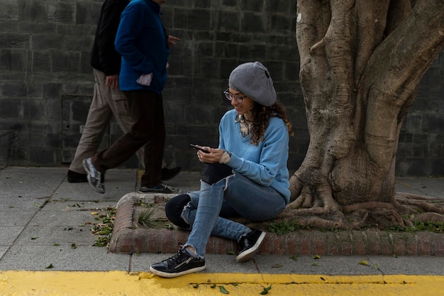 Jeune femme hipster latino-américaine assise sur le trottoir en lisant un livre numérique