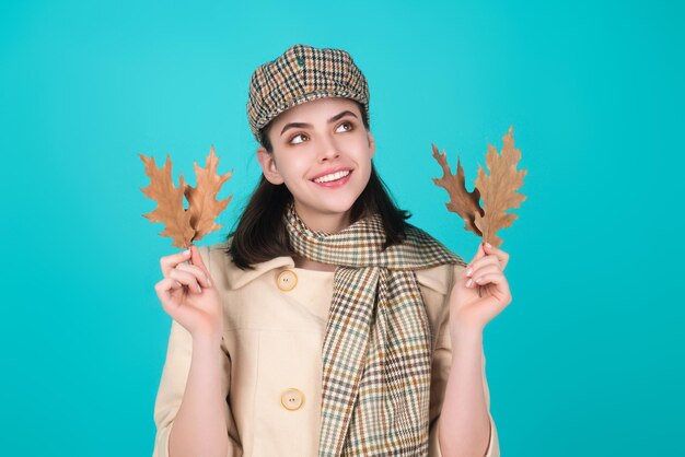 Une jeune femme hipster en tenue d'automne à la mode, un chapeau et une écharpe élégants, une belle fille tenant des feuilles d'autumn près du visage isolé sur le fond du studio, portrait d'une femme automnale avec une feuille d'érable.