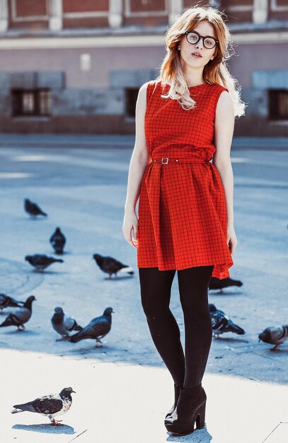 Jeune femme hipster vêtue d'une robe rouge dans la ville. Printemps et oiseaux colombes.