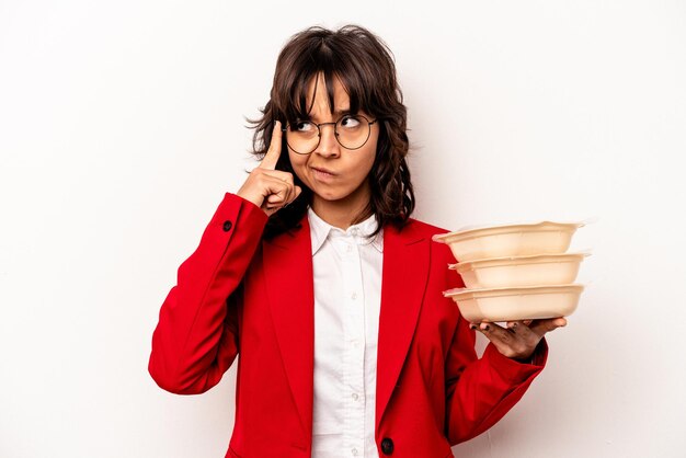 Jeune femme hispanique d'affaires tenant tupperware isolé sur fond blanc pointant le temple avec la pensée du doigt concentrée sur une tâche