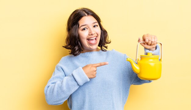 jeune femme hispanique à l'air excitée et surprise en pointant sur le côté. notion de théière