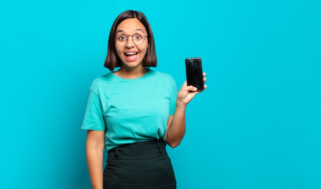 Jeune femme hispanique à l'air heureuse et agréablement surprise, excitée par une expression fascinée et choquée