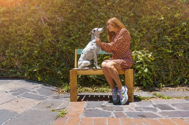 Jeune femme hispanique assise sur un banc avec son chien dans un parc