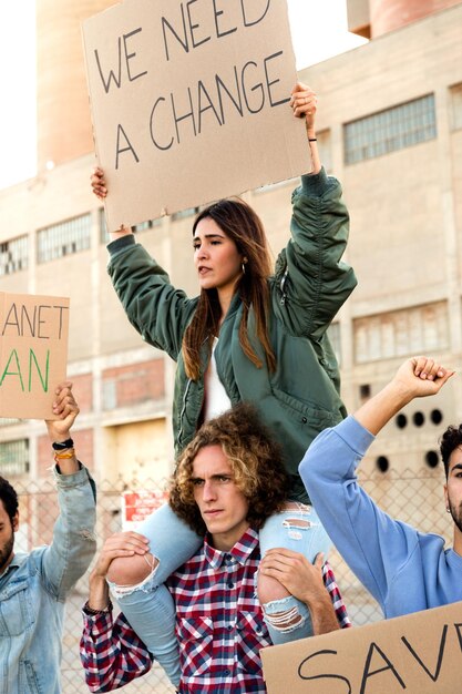 Jeune femme hispanique assise sur l'épaule de l'homme pour protester contre le changement climatique en démonstration Image verticale Concept activiste