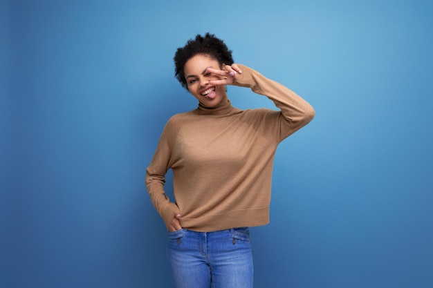 Jeune femme hispanique authentique aux cheveux bouclés afro dans des vêtements décontractés posant sur fond avec