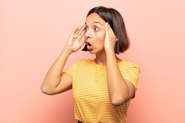 Jeune femme hispanique avec la bouche ouverte, l'air horrifié et choqué à cause d'une terrible erreur, levant les mains contre la tête