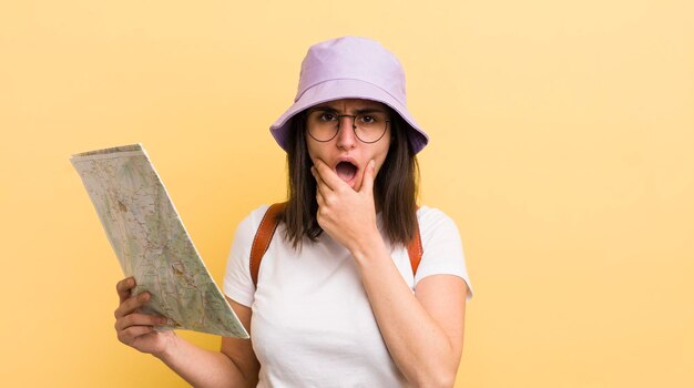 Jeune femme hispanique avec la bouche et les yeux grands ouverts et la main sur le concept touristique et de carte du menton