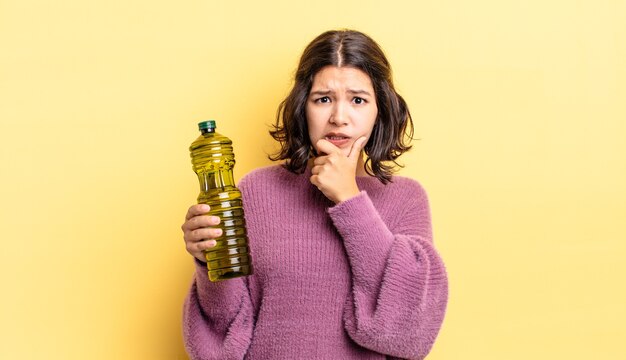 Jeune femme hispanique avec la bouche et les yeux grands ouverts et la main sur le menton. concept d'huile d'olive