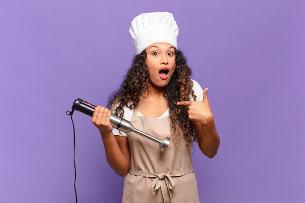 Jeune femme hispanique à la choqué et surpris avec la bouche grande ouverte, pointant vers soi. concept de chef