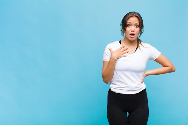 Jeune femme hispanique choquée, étonnée et surprise, la main sur la poitrine et la bouche ouverte, disant qui, moi?