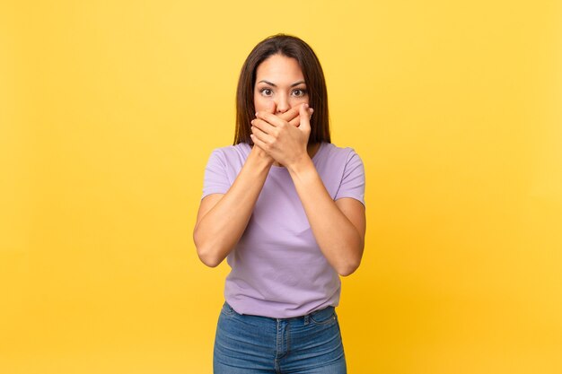 Jeune femme hispanique couvrant la bouche avec les mains avec un choc