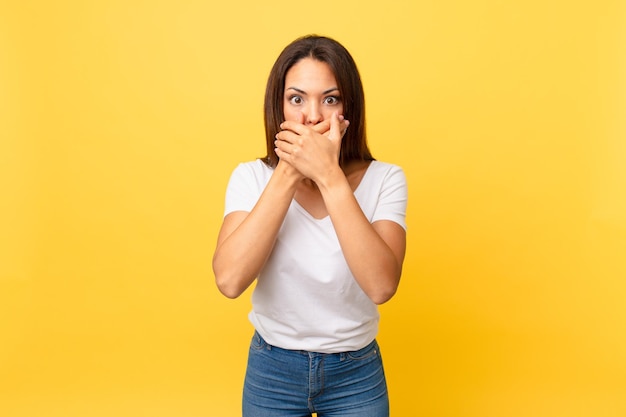 Jeune femme hispanique couvrant la bouche avec les mains avec un choqué