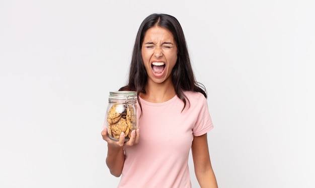 jeune femme hispanique criant agressivement, l'air très en colère et tenant une bouteille en verre de cookies