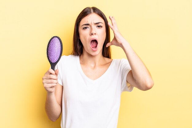 Jeune femme hispanique criant avec les mains en l'air. concept de brosse à cheveux