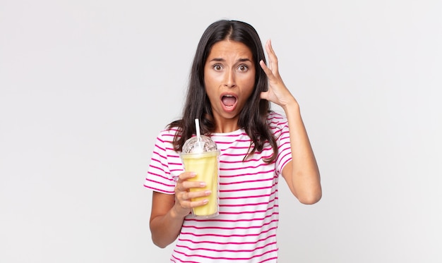 Jeune femme hispanique criant avec les mains en l'air et tenant un milk-shake à la vanille