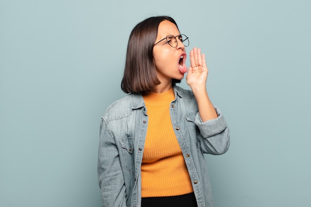 Jeune femme hispanique crier fort et en colère pour copier l'espace sur le côté, avec la main à côté de la bouche