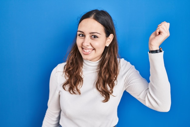 Jeune femme hispanique debout sur fond bleu dansant heureux et joyeux souriant se déplaçant décontracté et confiant en écoutant de la musique