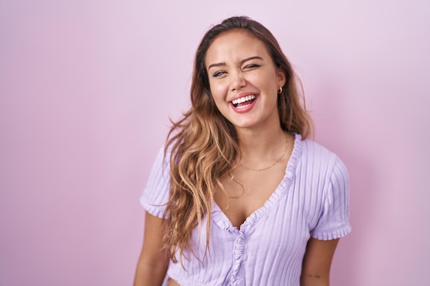 Jeune femme hispanique debout sur fond rose en regardant la caméra avec une expression sexy, un visage joyeux et heureux.