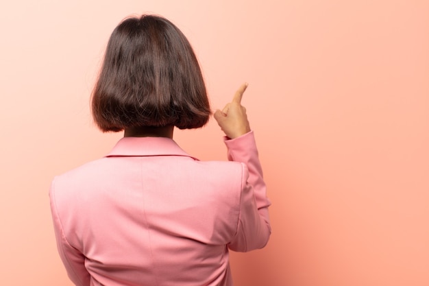 Jeune femme hispanique debout et pointant vers l'objet sur l'espace de copie, vue arrière