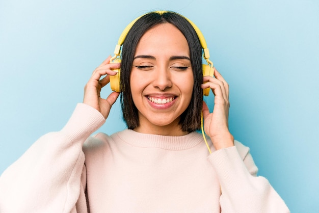 Jeune femme hispanique écoutant de la musique isolée sur fond bleu