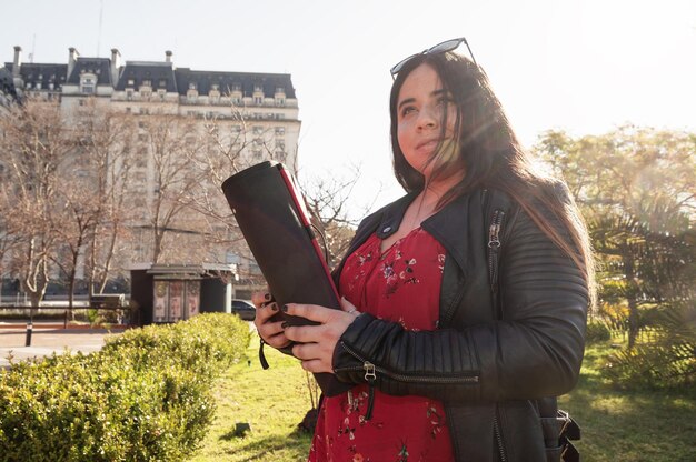 Jeune femme hispanique étudiante à l'université latine avec son classeur dans les mains à l'extérieur dans un jardin de la ville